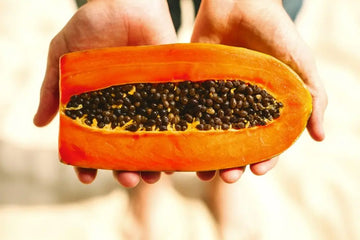 Mann hält eine halbierte Papaya mit schwarzen Kernen