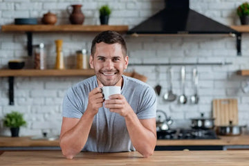 Mann sitzt mit einer Tasse Kräutertee am Küchentisch